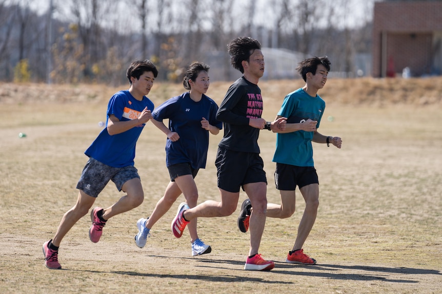 Three Japanese teens and a man running around a dusty track 