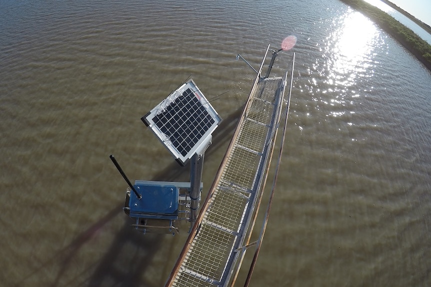 A solar panel and radar device suspended over the water on a flood plain harvesting storage dam.