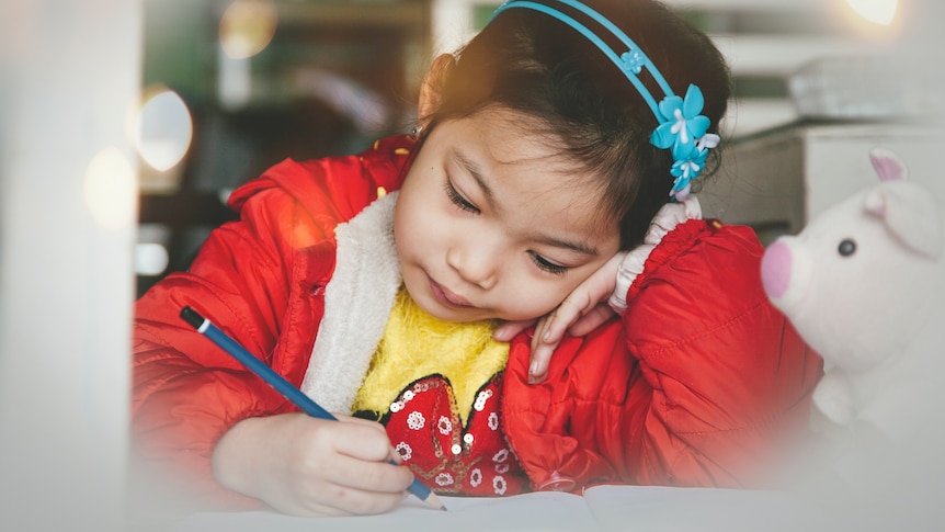 A young girl concentrates as she writes with a pencil