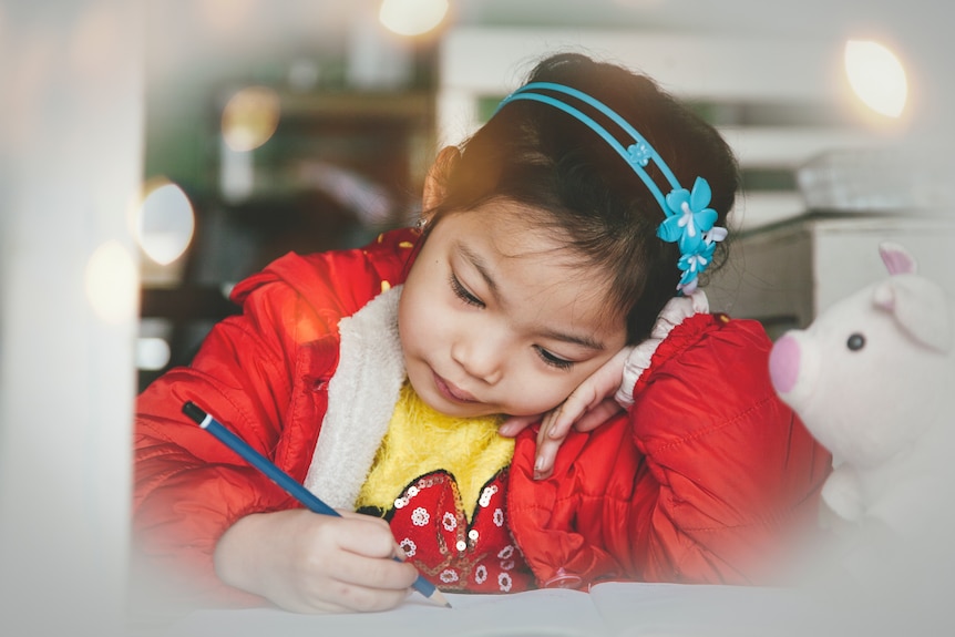 A young girl concentrates as she writes with a pencil