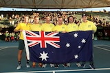Australia's winning Davis Cup team stand on court holding an Australian flag in front of them.