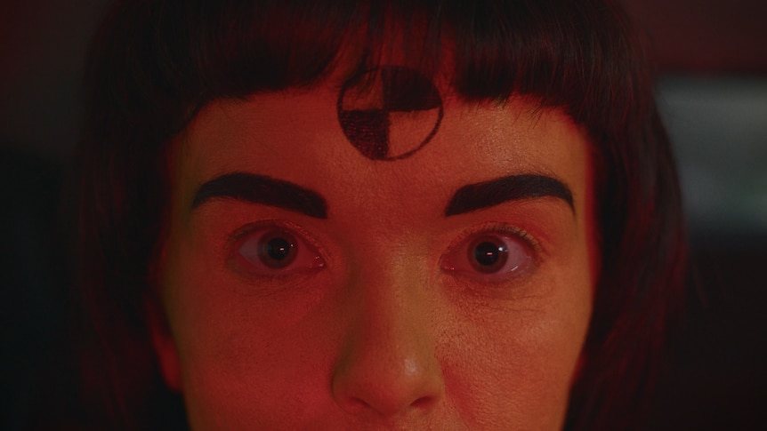 close up of a woman's face with a crash test dummy symbol painted on her forehead