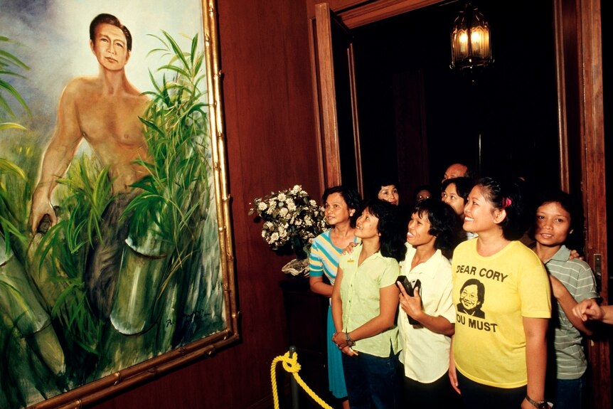 A group of Filipino women look at a painting of a shirtless man cutting sugar cane. The painting isn't that good