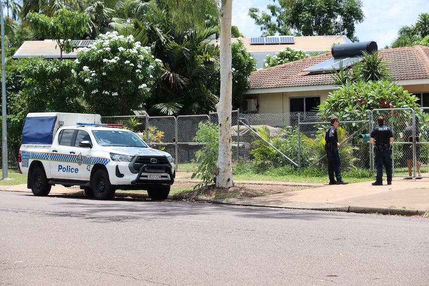 A police car parked outside a property as two officers speak to a resident in the front yard.