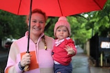 A woman and a young child with jumpers on standing on a path holding an umbrella. 