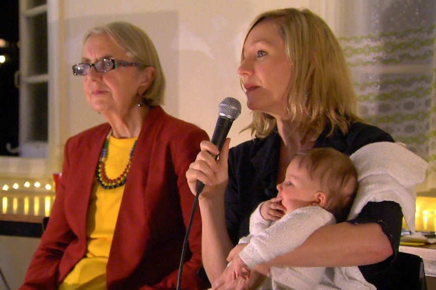 Greens Senator Lee Rhiannon with Larissa Waters, who is holding her baby and speaking into a microphone.