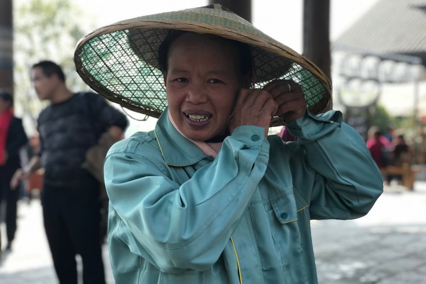 A woman ties the strap of a wide-brimmed hat under her chin.