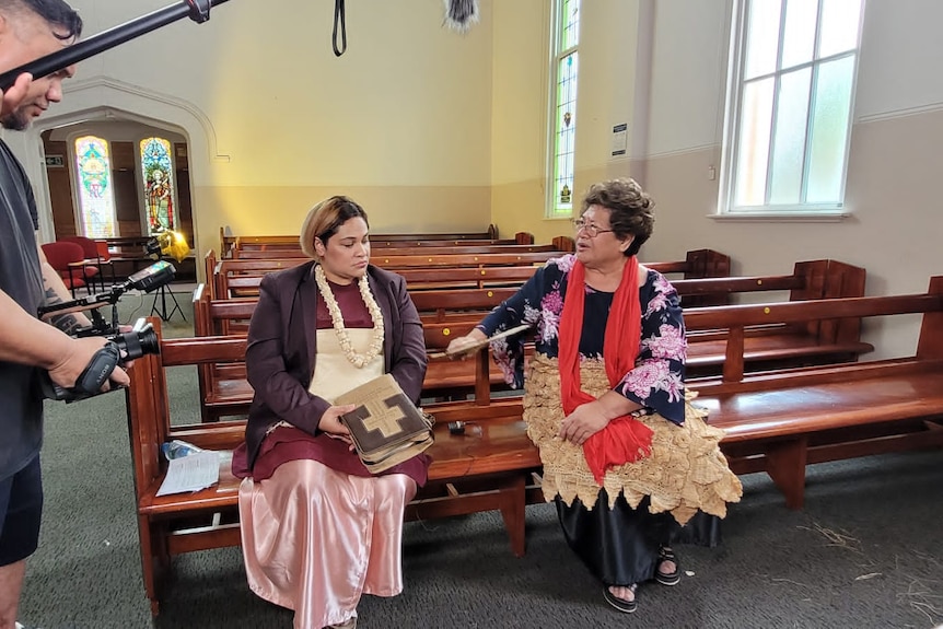 Two women sit at church as camera's film.