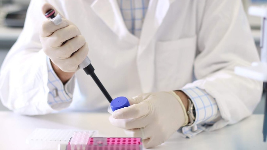 A scientist in a lab coat holds a needle in a lab.