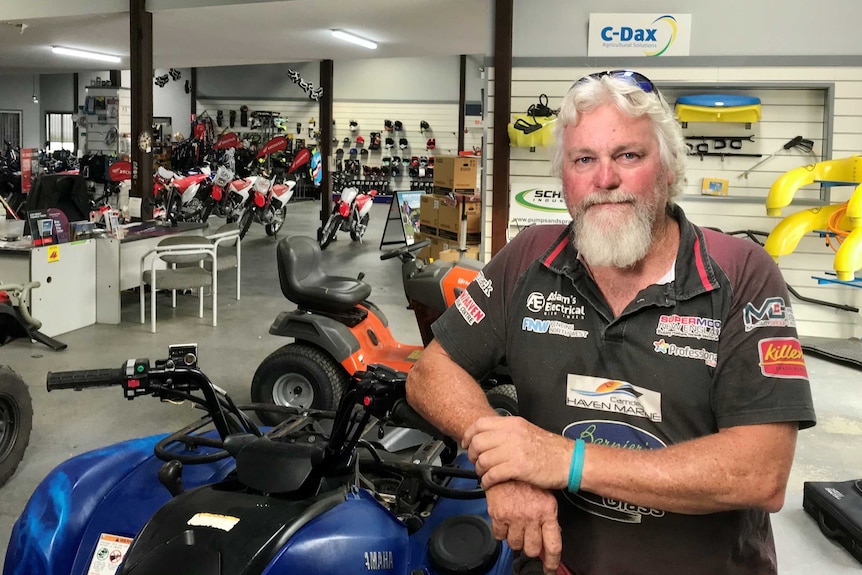 Greg Frost stands in a shop with motorbikes behind him.