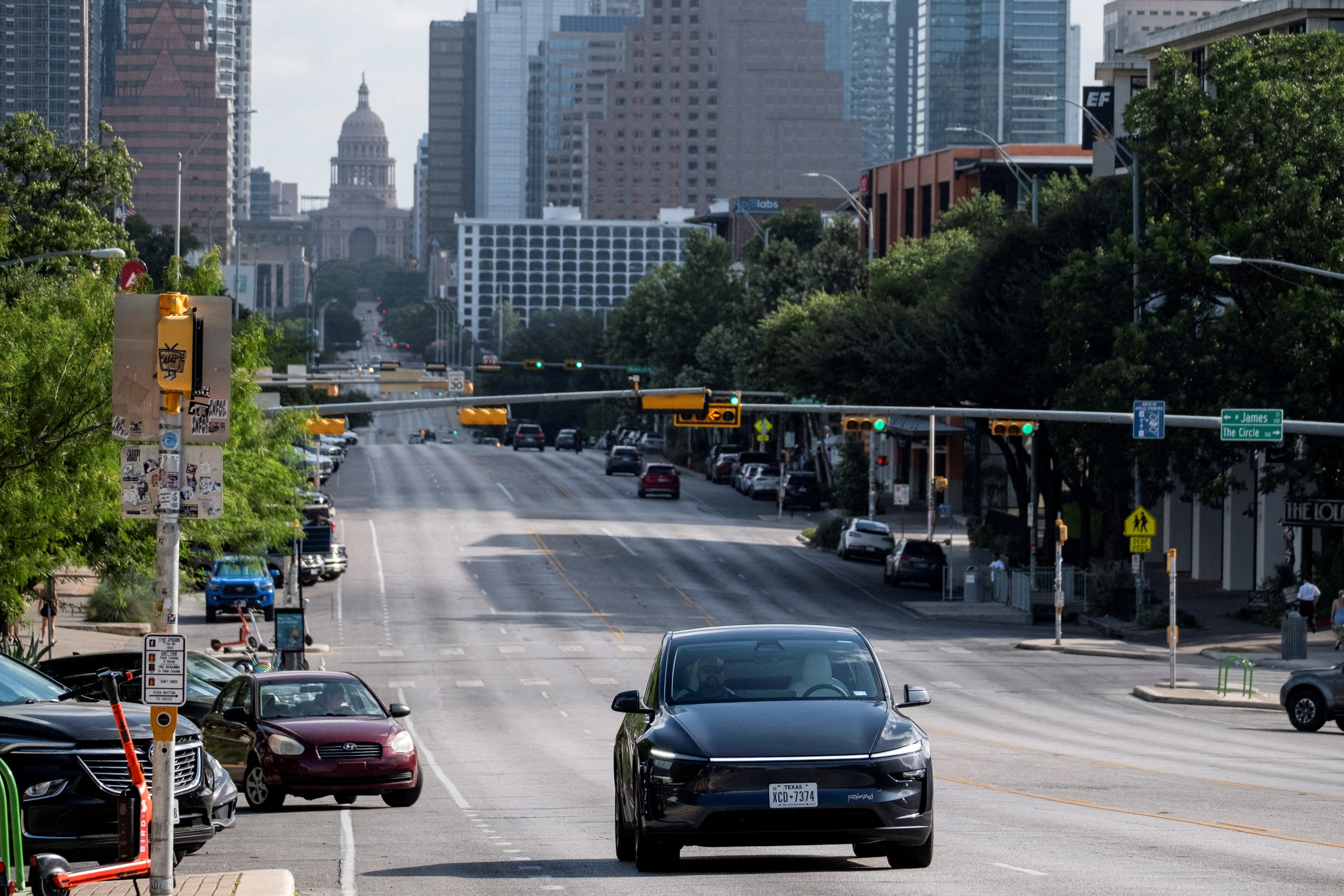 A black Tesla car drives down a wide city road. No driver sits behind the steering wheel
