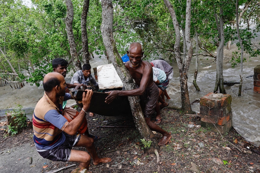 A group of men pull a wooden boat from a river, taking it to higher ground before a cyclone arrives.