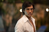 Tahar Rahim in a 70s style white shirt and glasses.