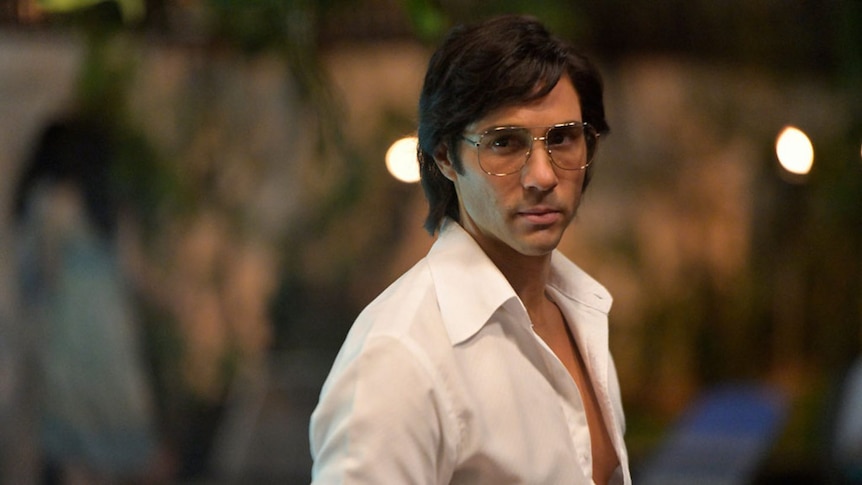 Tahar Rahim in a 70s style white shirt and glasses.