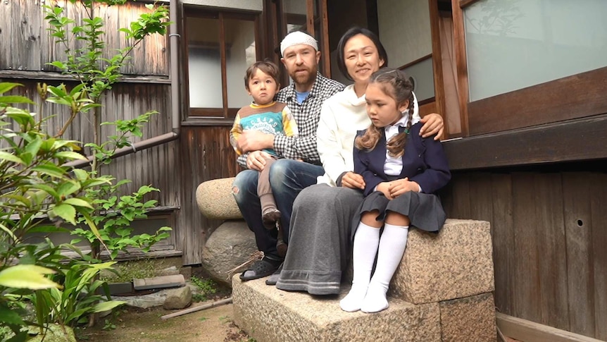 A father, mother, young daughter and son sit in the courtyard of their Japanese home.