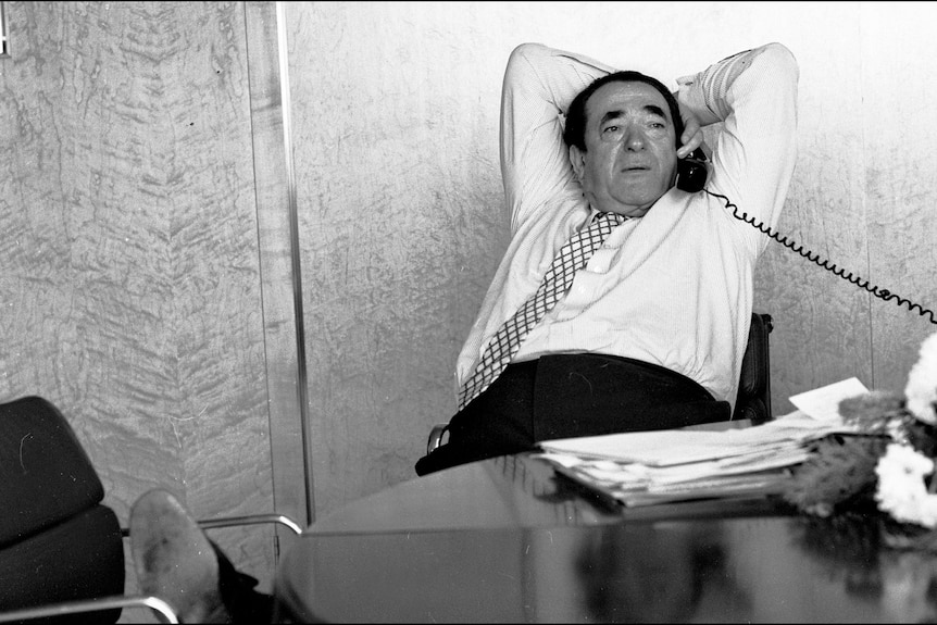 A black and white photo of Robert Maxwell reclining at his desk while on the telephone