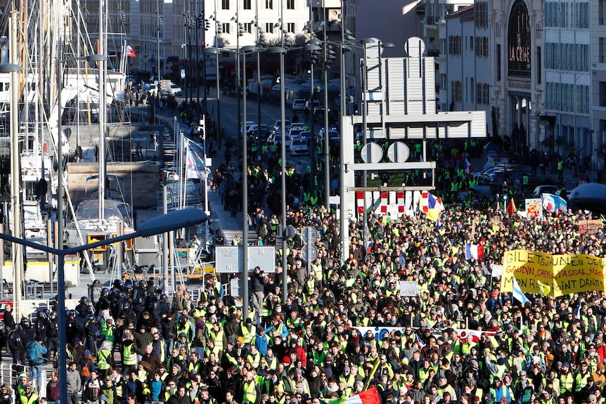 An aerial photo of a road running through Marseille's old harbour shows a large crowd of protesters marching with bright signs.