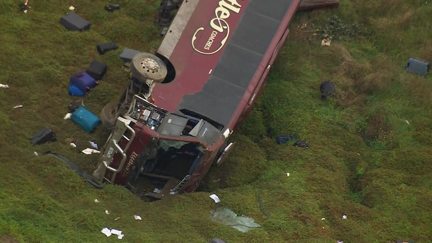 large burgundy coloured bus comes to a stop down embankment after collision