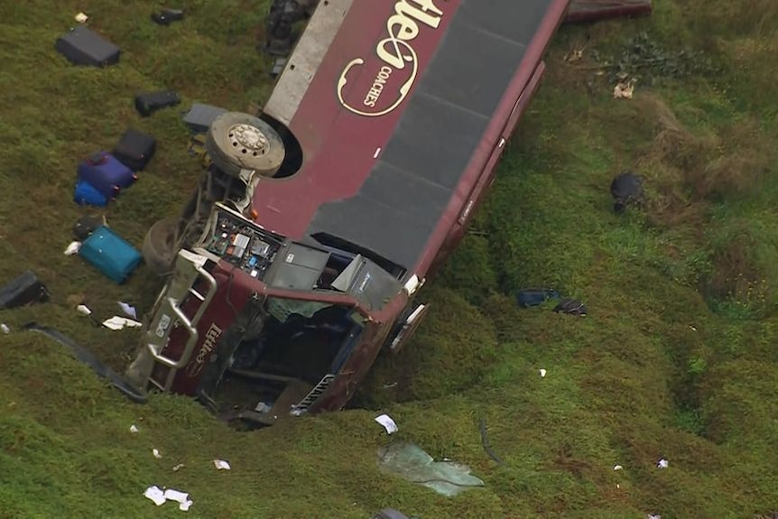 large burgundy coloured bus comes to a stop down embankment after collision