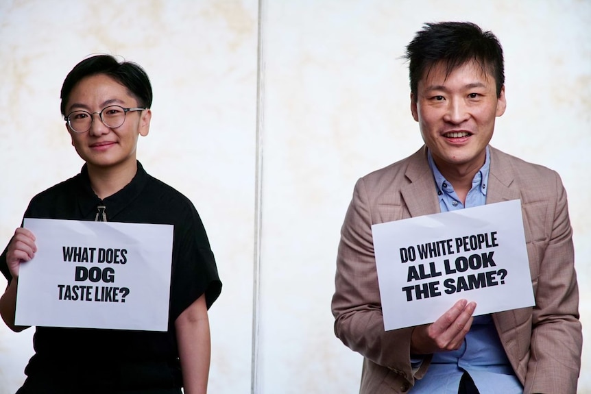 JInghua Qian and Kristian Chong hold placards of "What does dog taste like" and "Do white people all look the same".