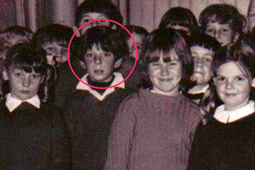 a boy stands among his classmates in an old picture