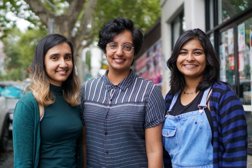 Three women with dark hair looking at the camera, smiling