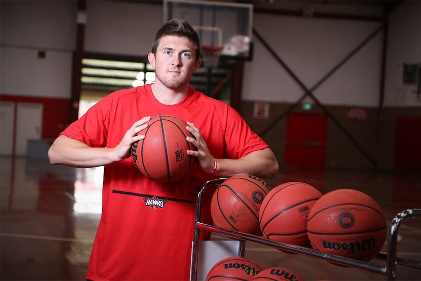 Rotnei Clarke stands on a basketball court holding a basketball.