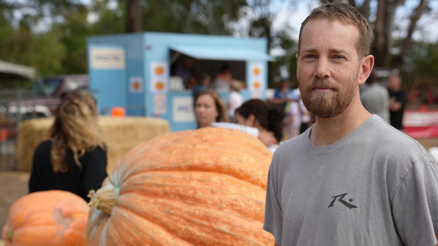a man in a great t shirt standing next to a pumpkin