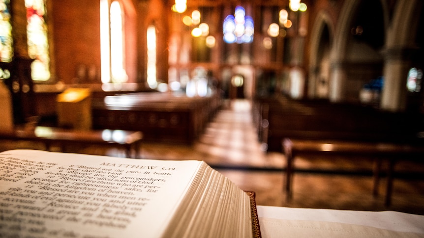 close of up bible corner in front of church pews and blurred stained glass windows