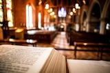 close of up bible corner in front of church pews and blurred stained glass windows