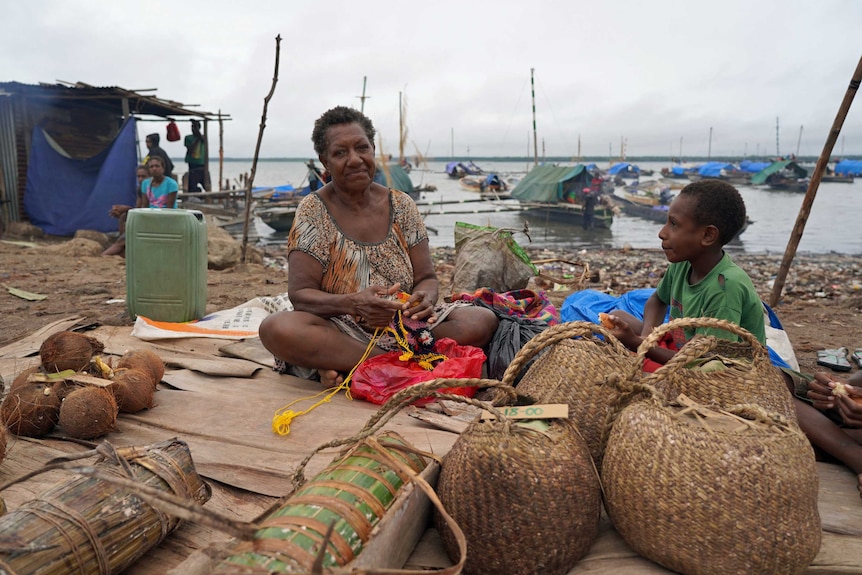 A woman and child sit on a mat on a beach.