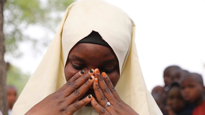 A girl wearing a yellow hijab holds her face