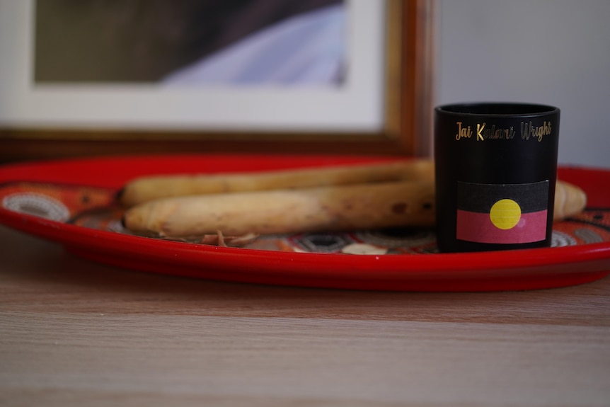 A candle with an aboriginal flag is sitting on top of an Aboriginal plate with clapping sticks