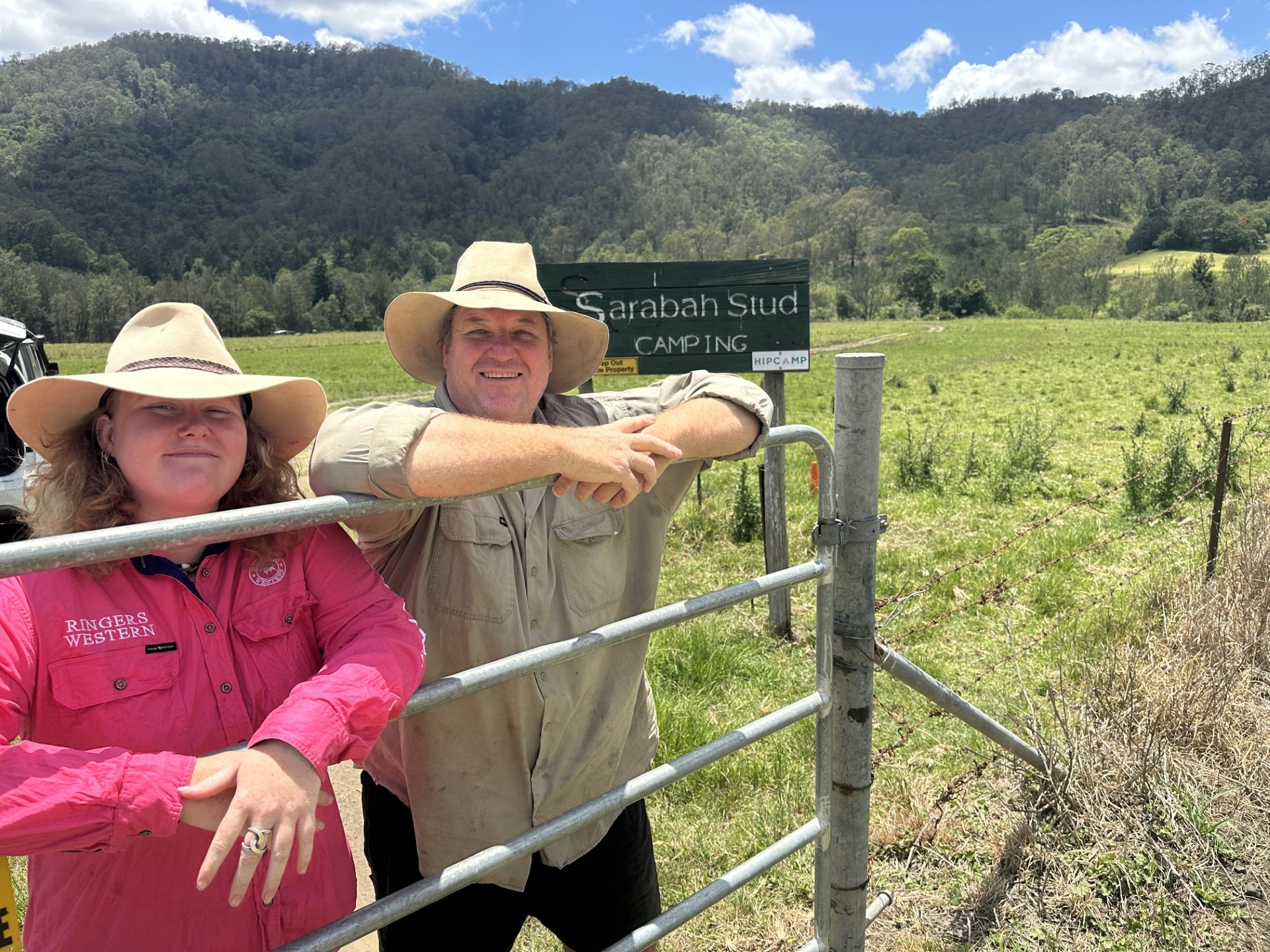 Mulher e homem encostados na cerca da fazenda