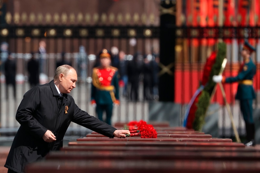 Vladimir Putin lays a wreath of red flowers on a casket
