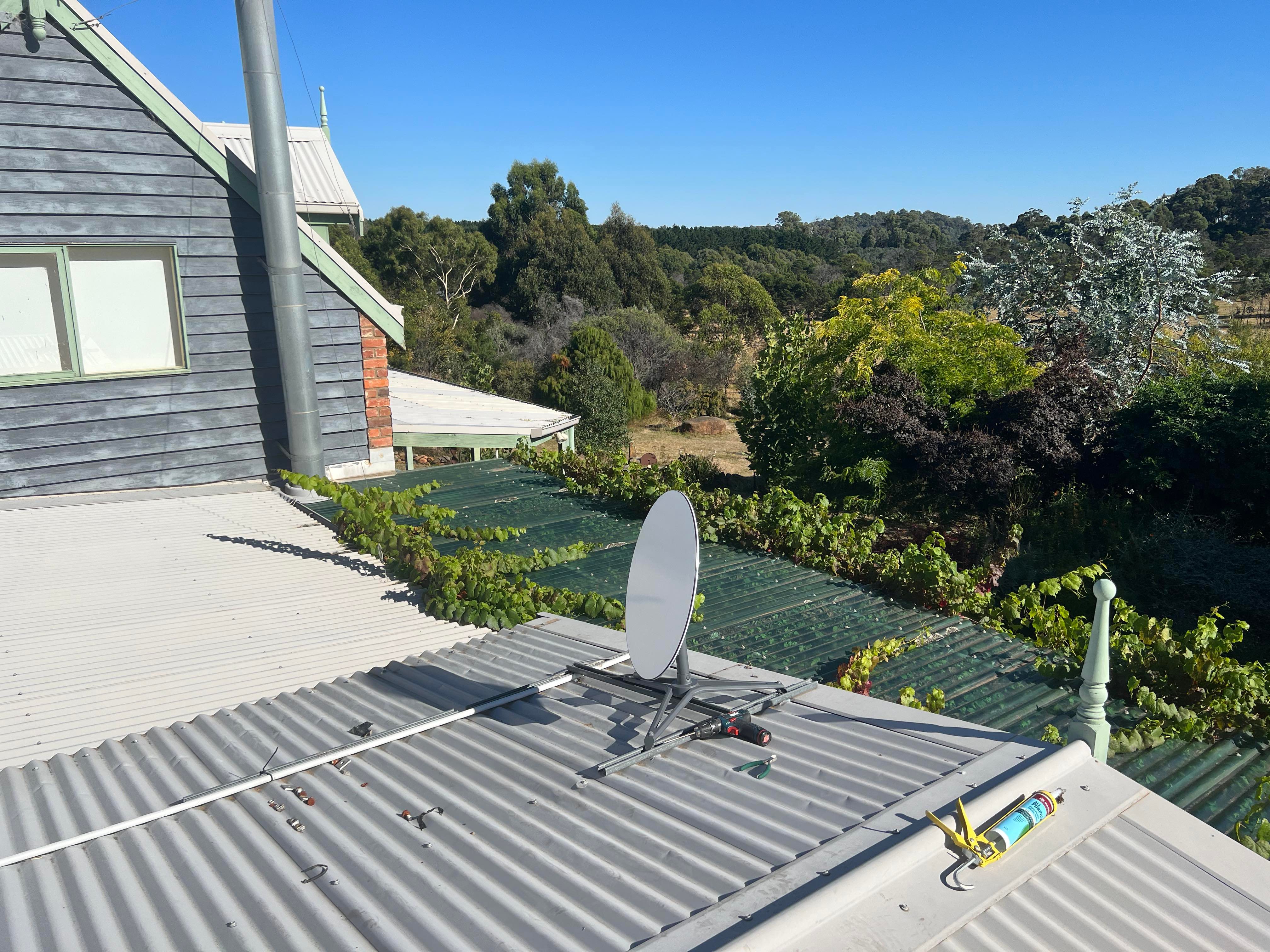 A satellite dish on a tin roof surrounded by trees