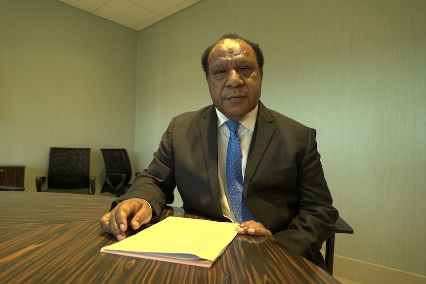 PNG Foreign Affairs Minister Rimbink Pato sits behind a desk and puts his hand next to a paper folder.