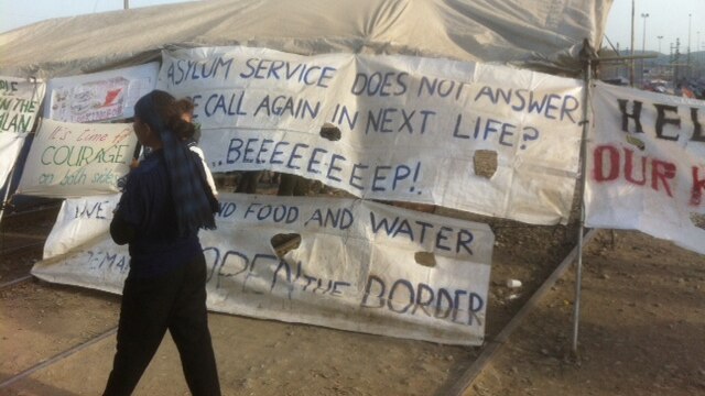 A woman and child walk past signs erected inside the Idomeni camp.