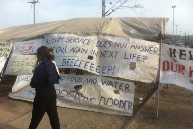 A woman and child walk past signs erected inside the Idomeni camp.