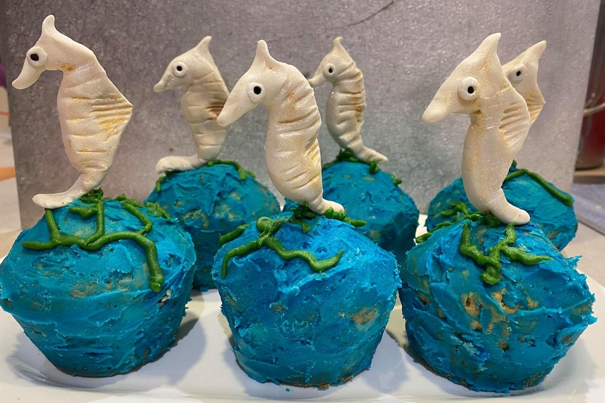 Blue iced cupcakes with white seahorse figures on top.