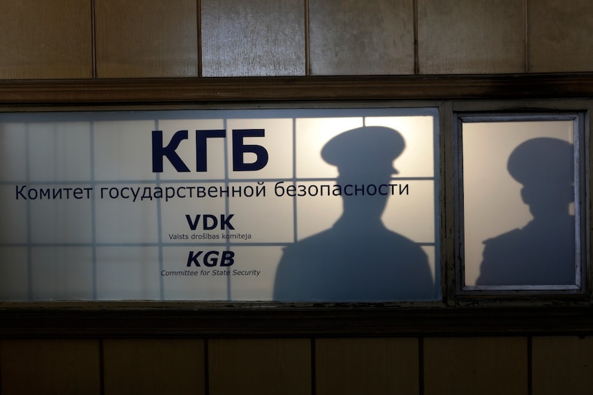 The silhouette of a man in uniform can be seen behind a window with a sign on it that says KGB on it 