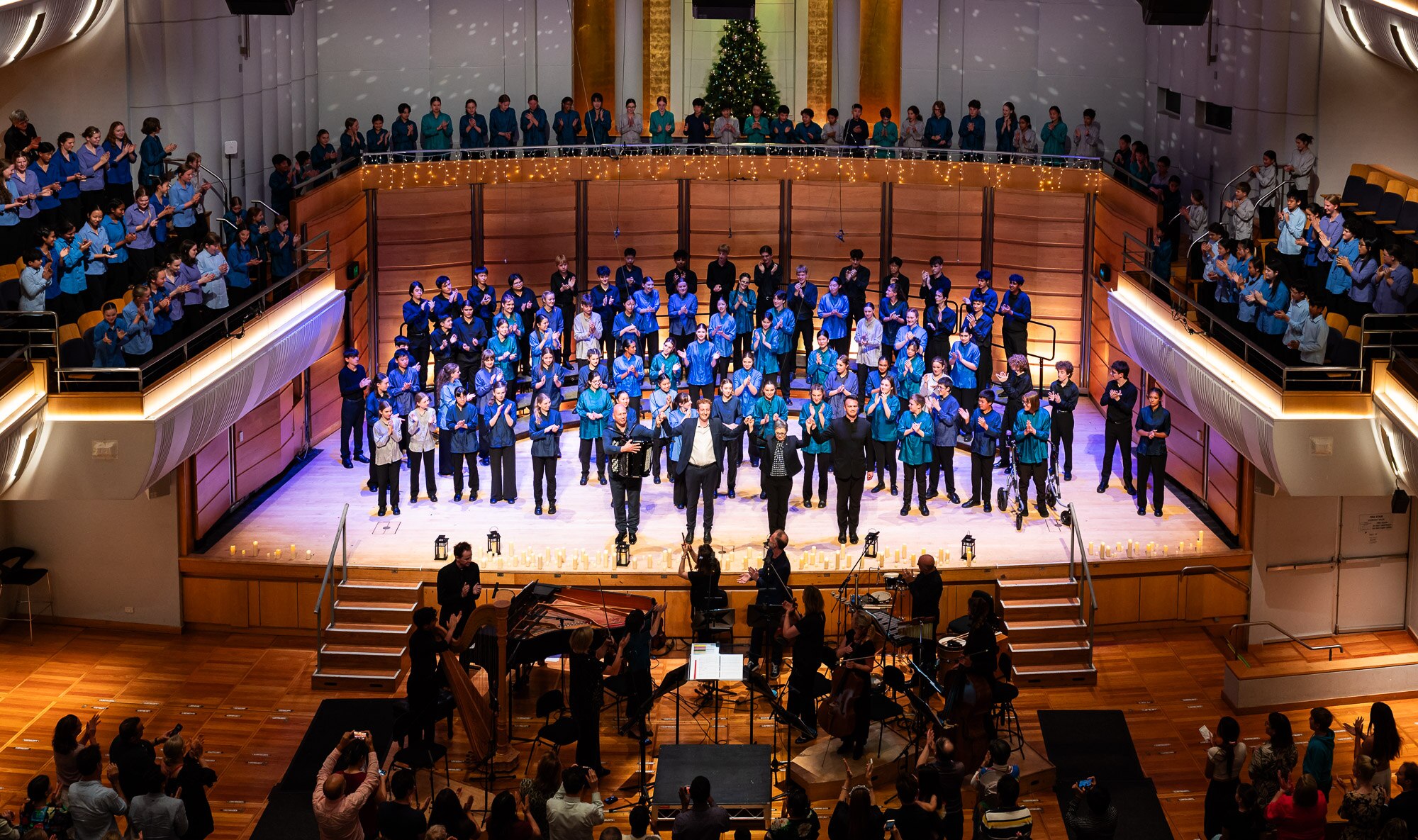 The stage and balcony at Angel Place is full of children dressed in a variety of blues and greens for their Christmas concert.