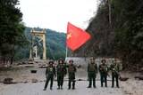 Soldiers with an MNDAA flag pose for a photo in front of a bridge.