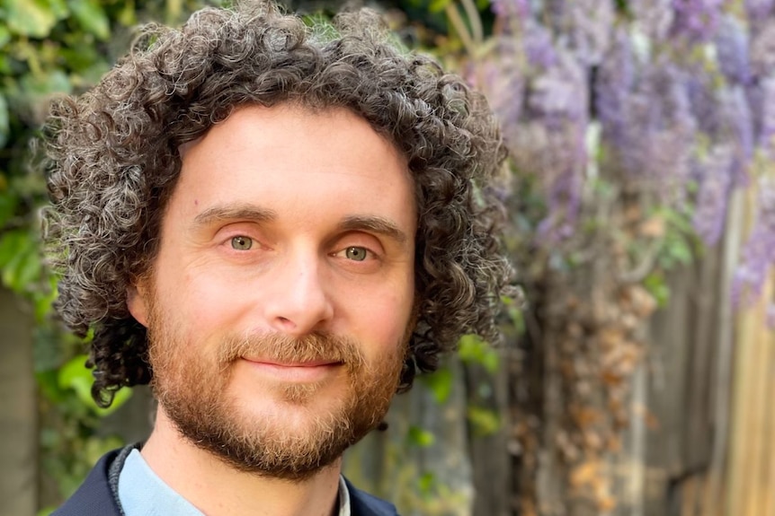 A smiling man in a suit with grey curly hair