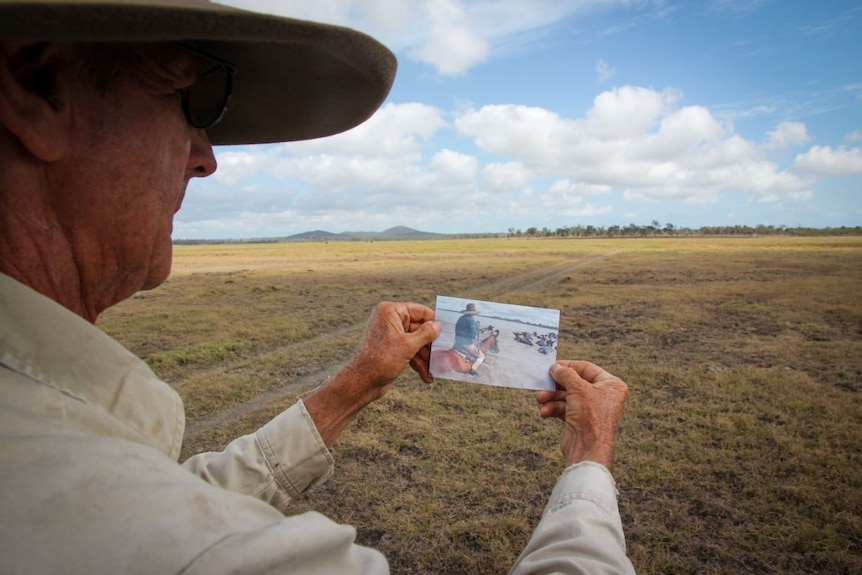 Back of man's head and hands holding a photograph with view of rural property in front of him