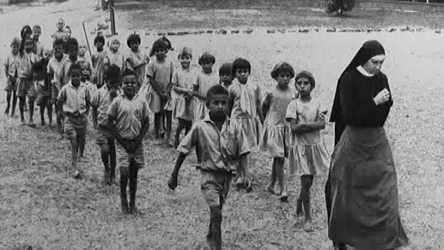 black and white photo of aboriginal children following a nun