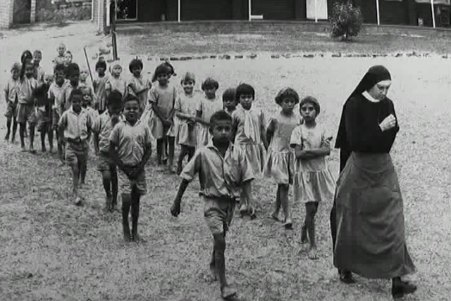 黑白照片显示，一名修女带着十多位原住民儿童行走