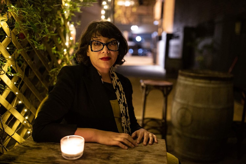 A woman sits at a table with a small candle in front of her.