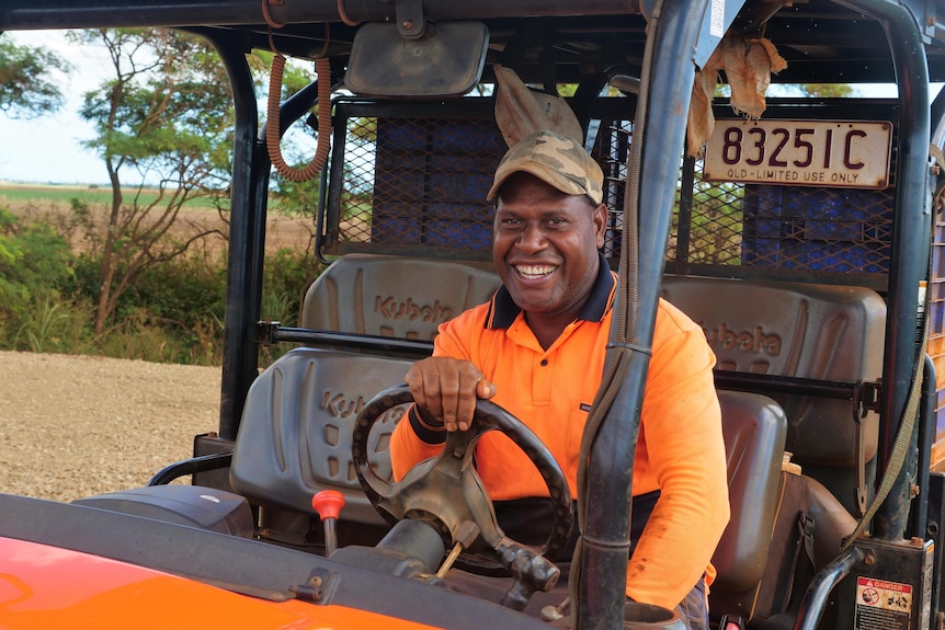 A ni-Vanuatu man in his 40s, wearing high-vis, sitting at the wheel of a farm buggy, smiling. 