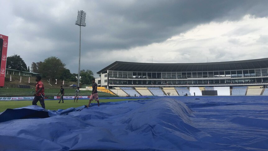 Groundsman apply covers as clouds roll in in Kandy